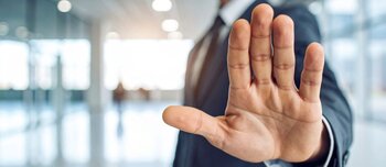 A man in a suit extends his hand with an open palm in a gesture of stopping or refusing. The person shows a clear signal of objection or denial in a professional setting
